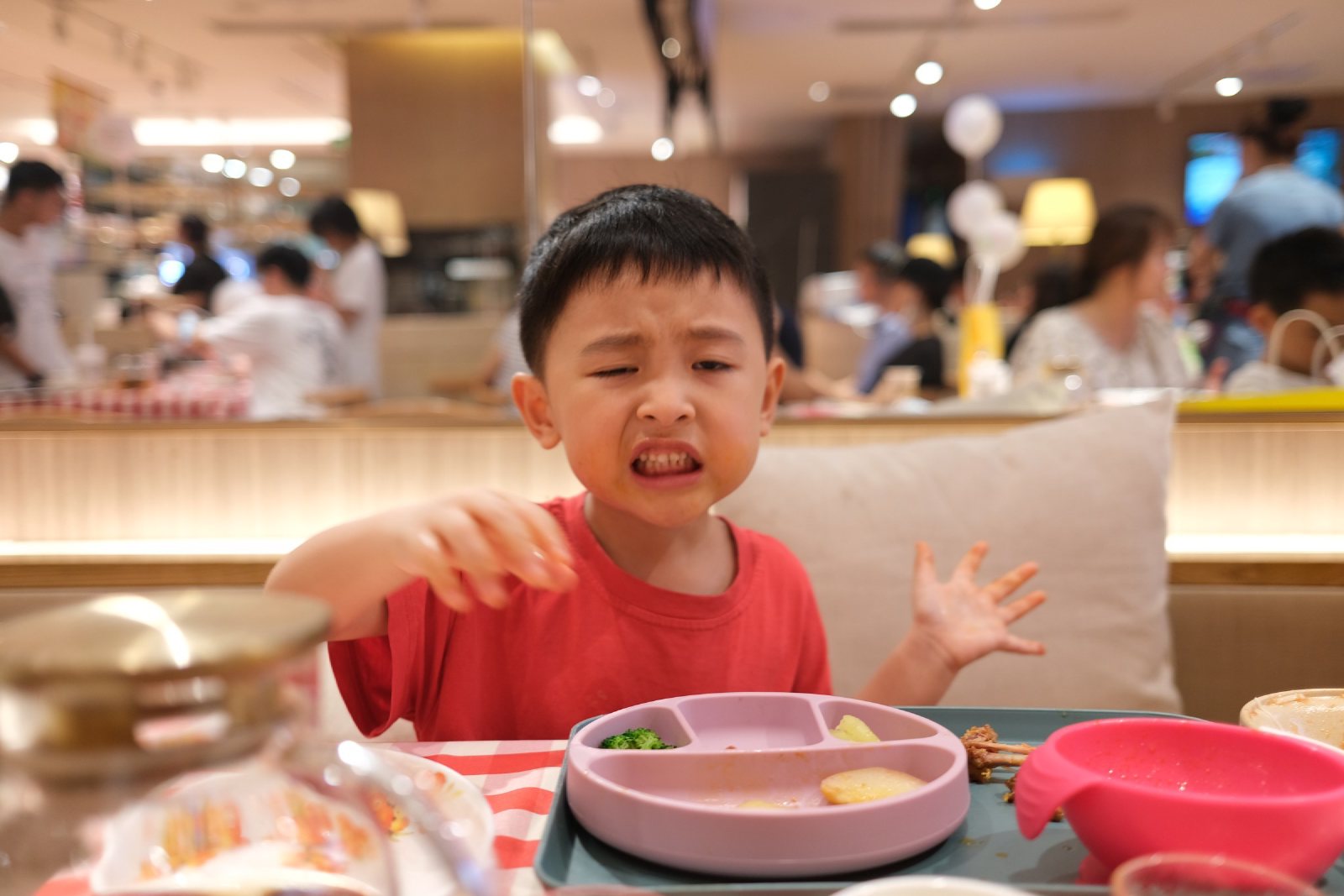 餐厅里儿子皱着脸伸出手，桌上是餐盘