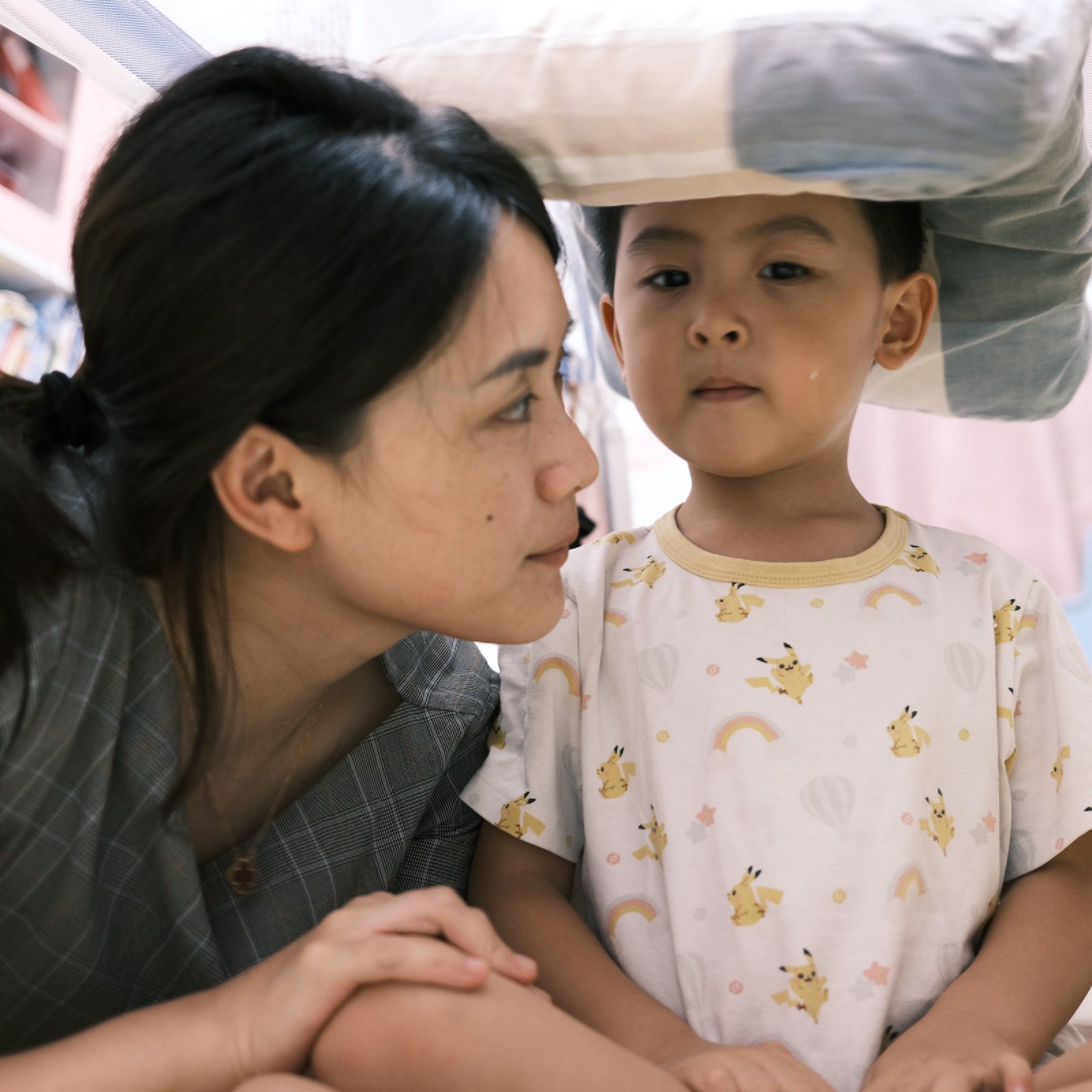 妈妈和儿子坐在床上，儿子头顶着枕头