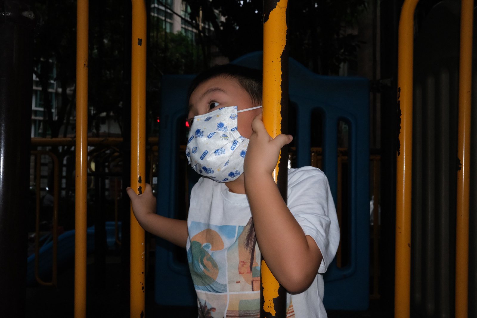 傍晚，戴口罩的儿子抓着游乐设施的栏杆