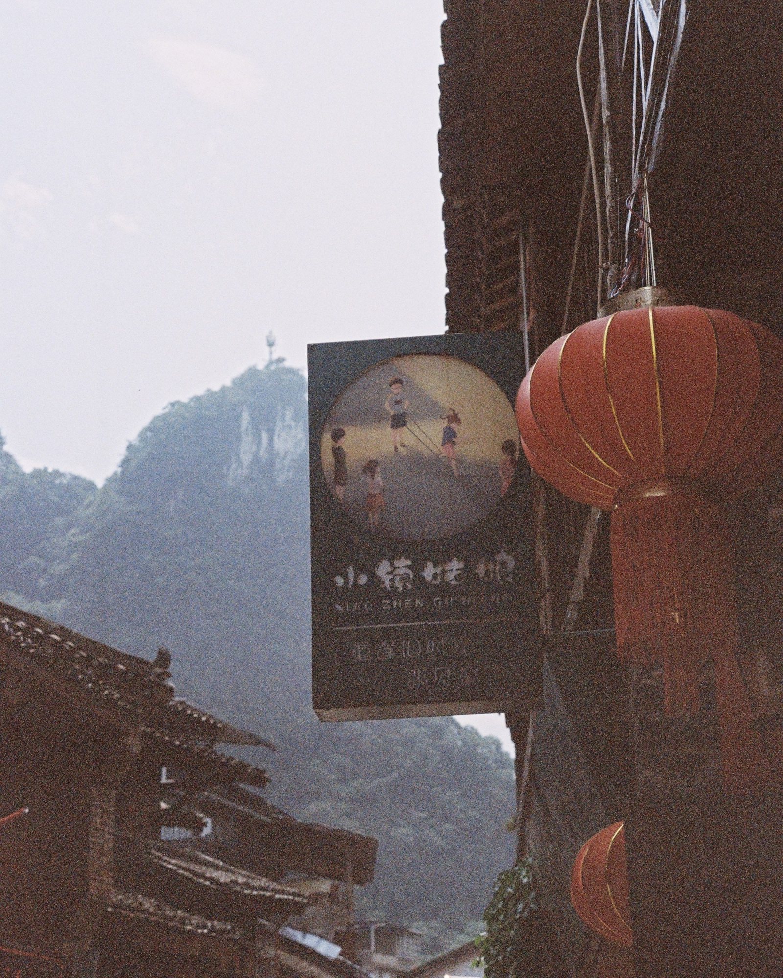老街屋檐下的红灯笼和招牌，远处是山