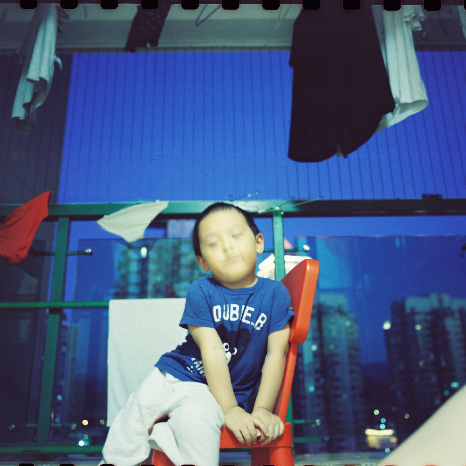 晚上,儿子坐在阳台的红色椅子上,背后是亮灯的楼