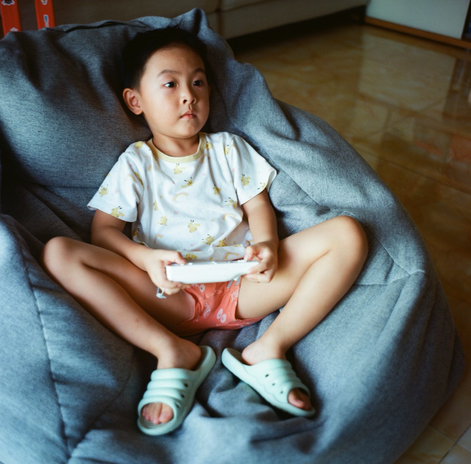 儿子盘腿坐在灰色懒人沙发里，拿着手柄
