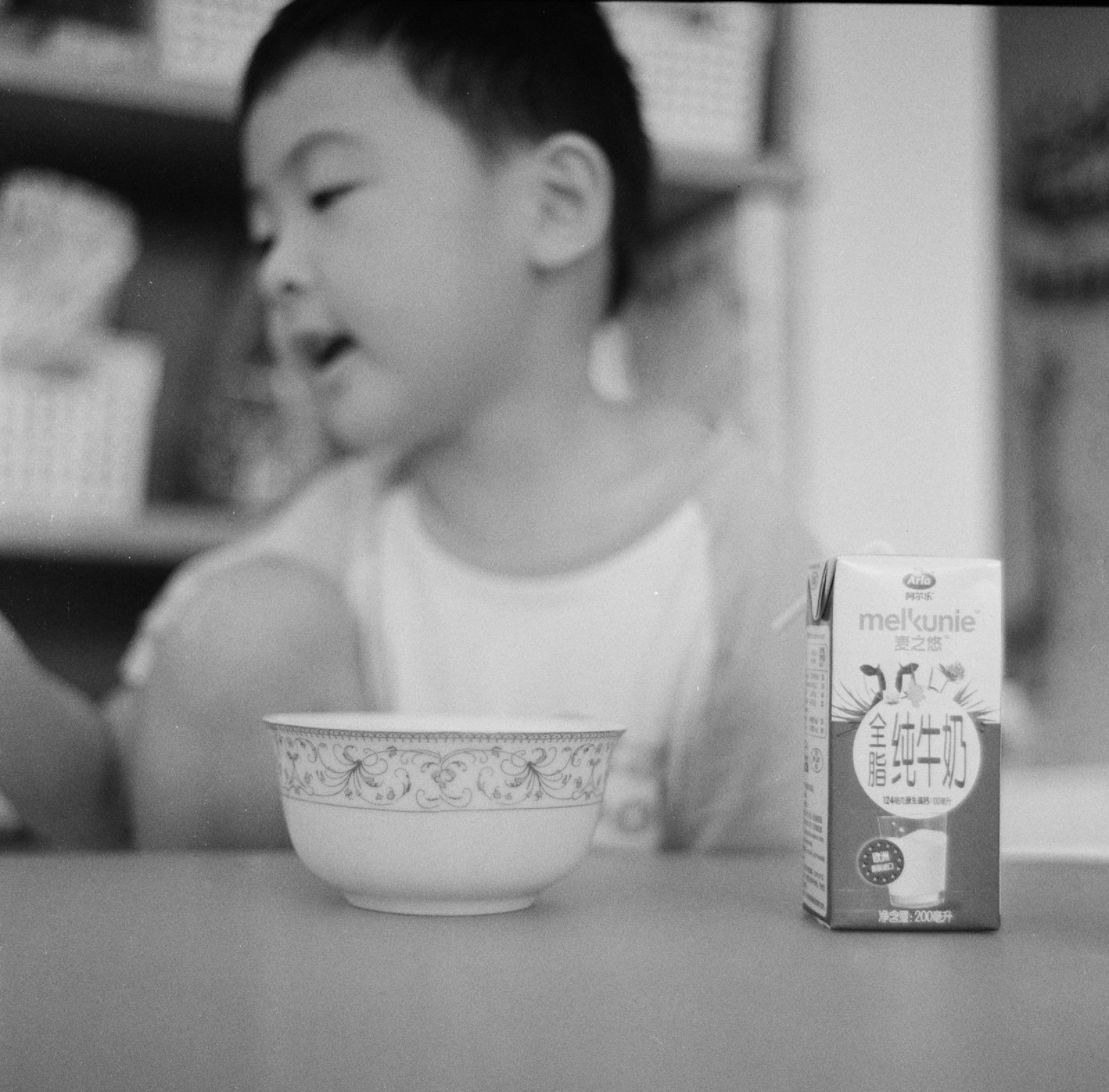 黑白，儿子坐在碗和牛奶后面，歪着嘴