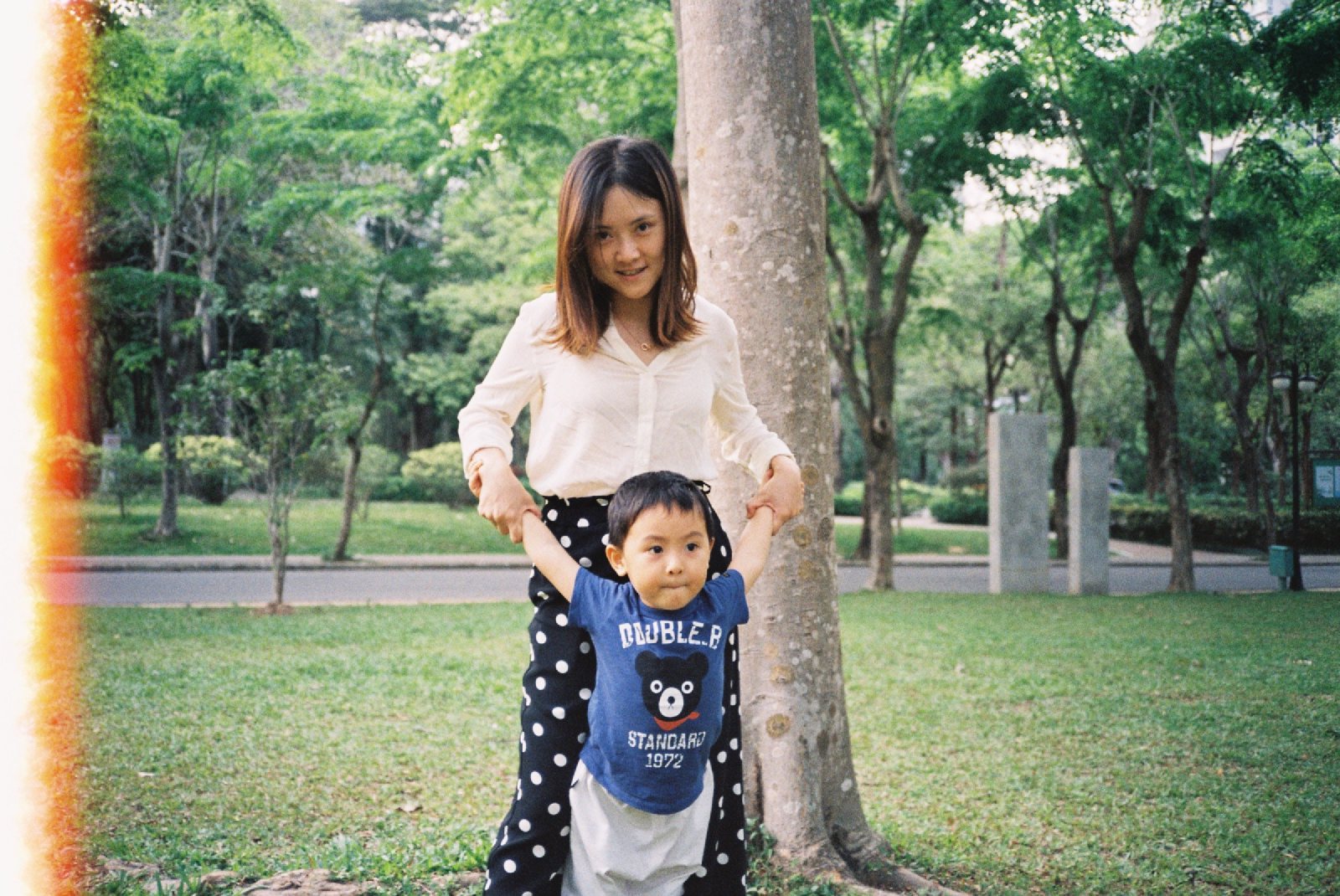 妈妈和儿子站在公园大树边，左边缘有一道漏光