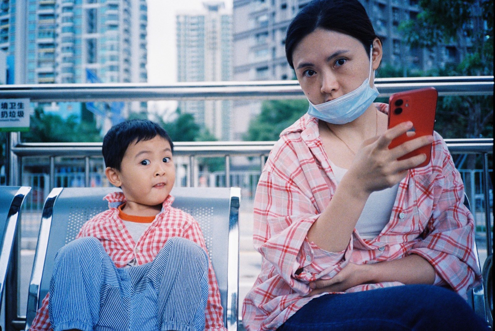 站台长椅上儿子瞪眼，妈妈拿着手机