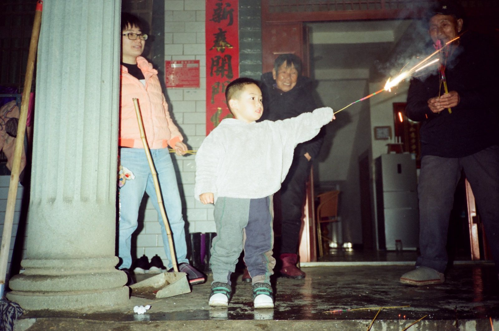 门廊柱子边，孩子伸手举着冒火的仙女棒