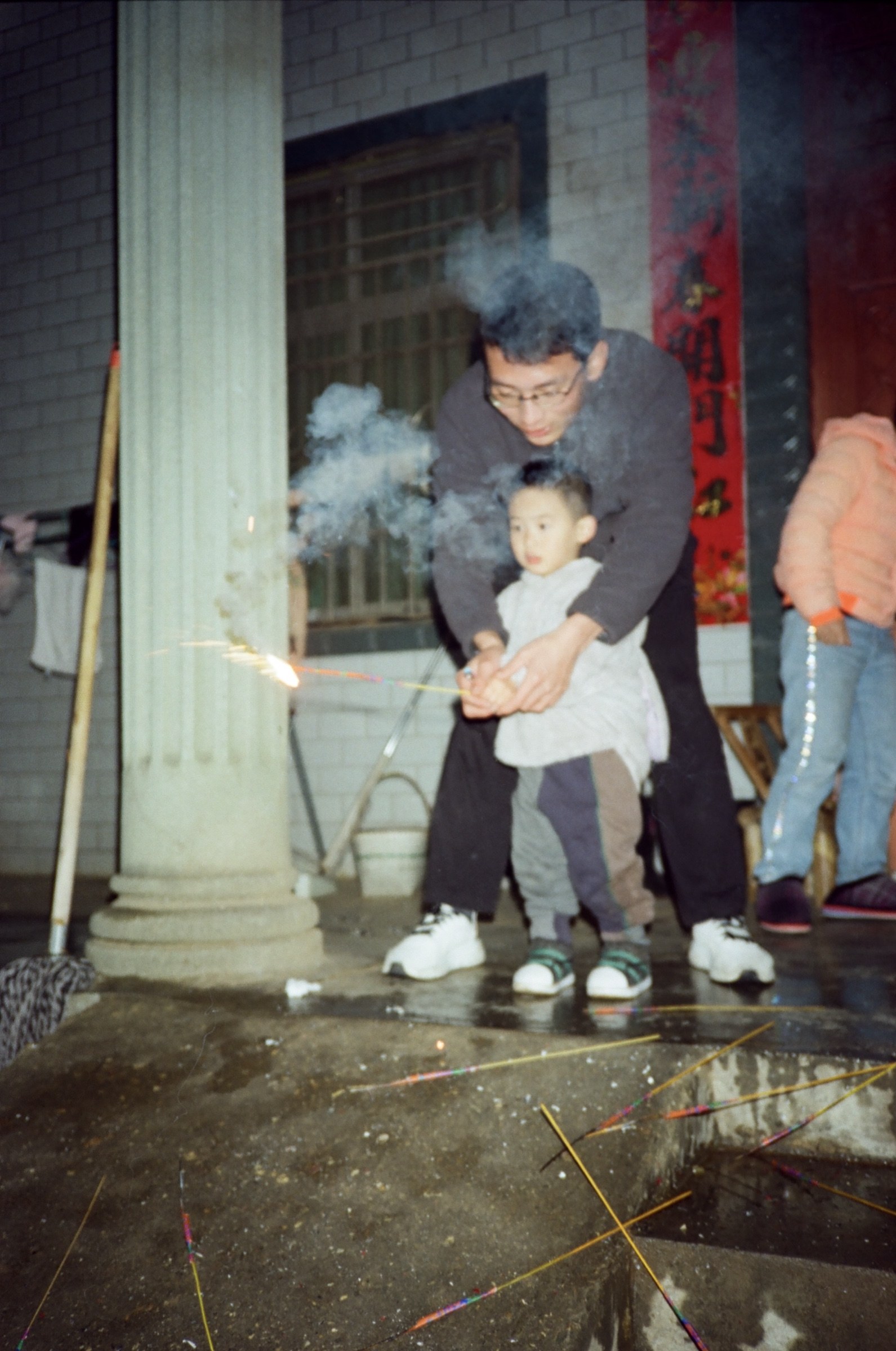 门廊下大人扶着儿子点仙女棒，烟雾弥漫
