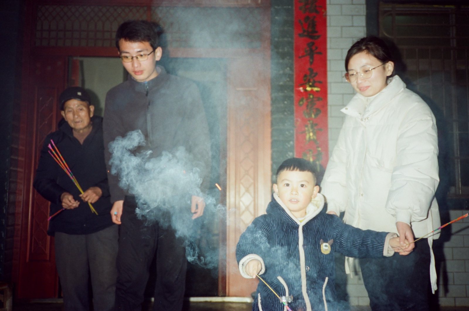 贴着春联的门口，儿子拿着仙女棒，亲戚们围着看