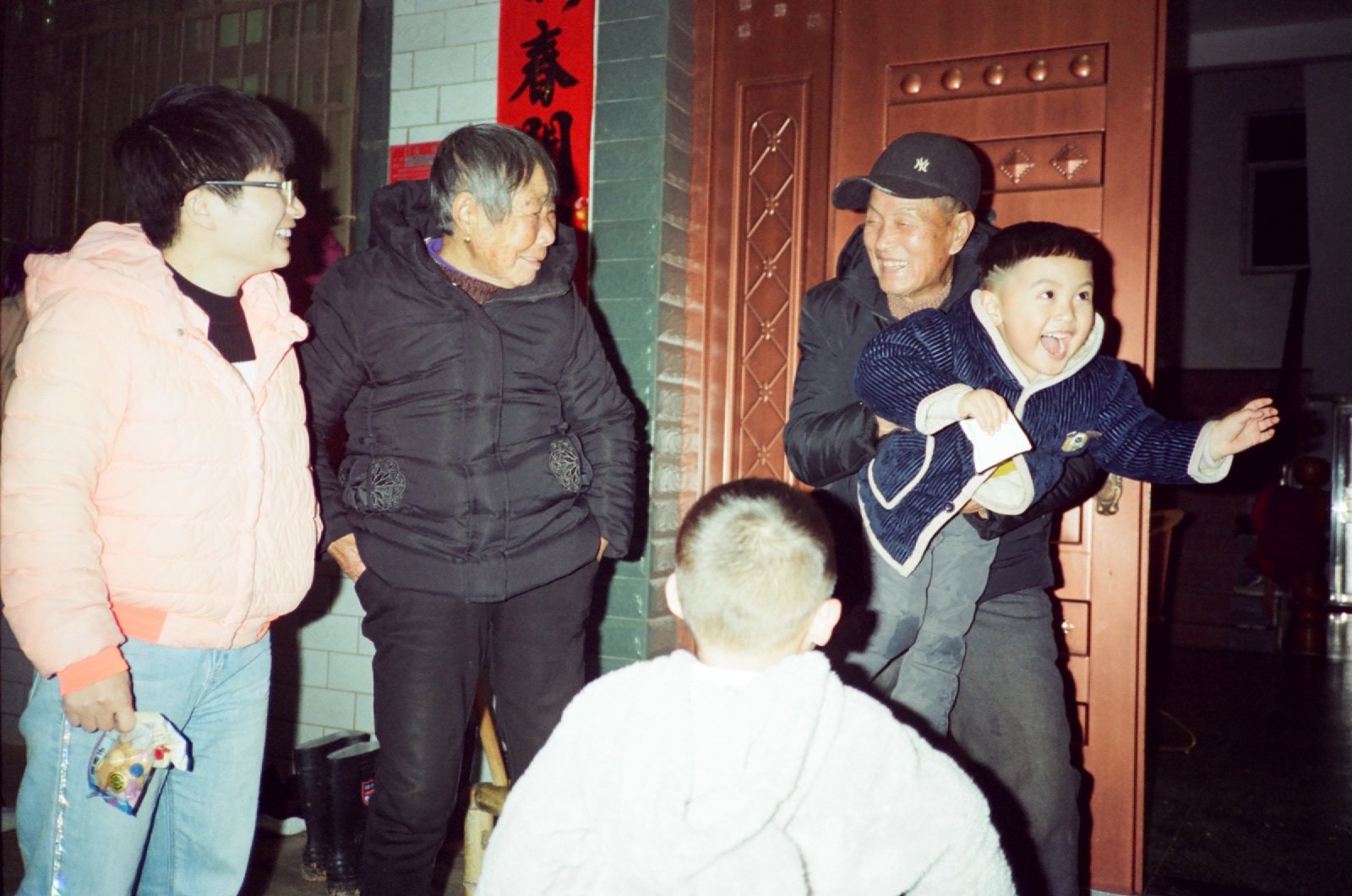 门口亲戚们笑着，儿子被抱起来大笑