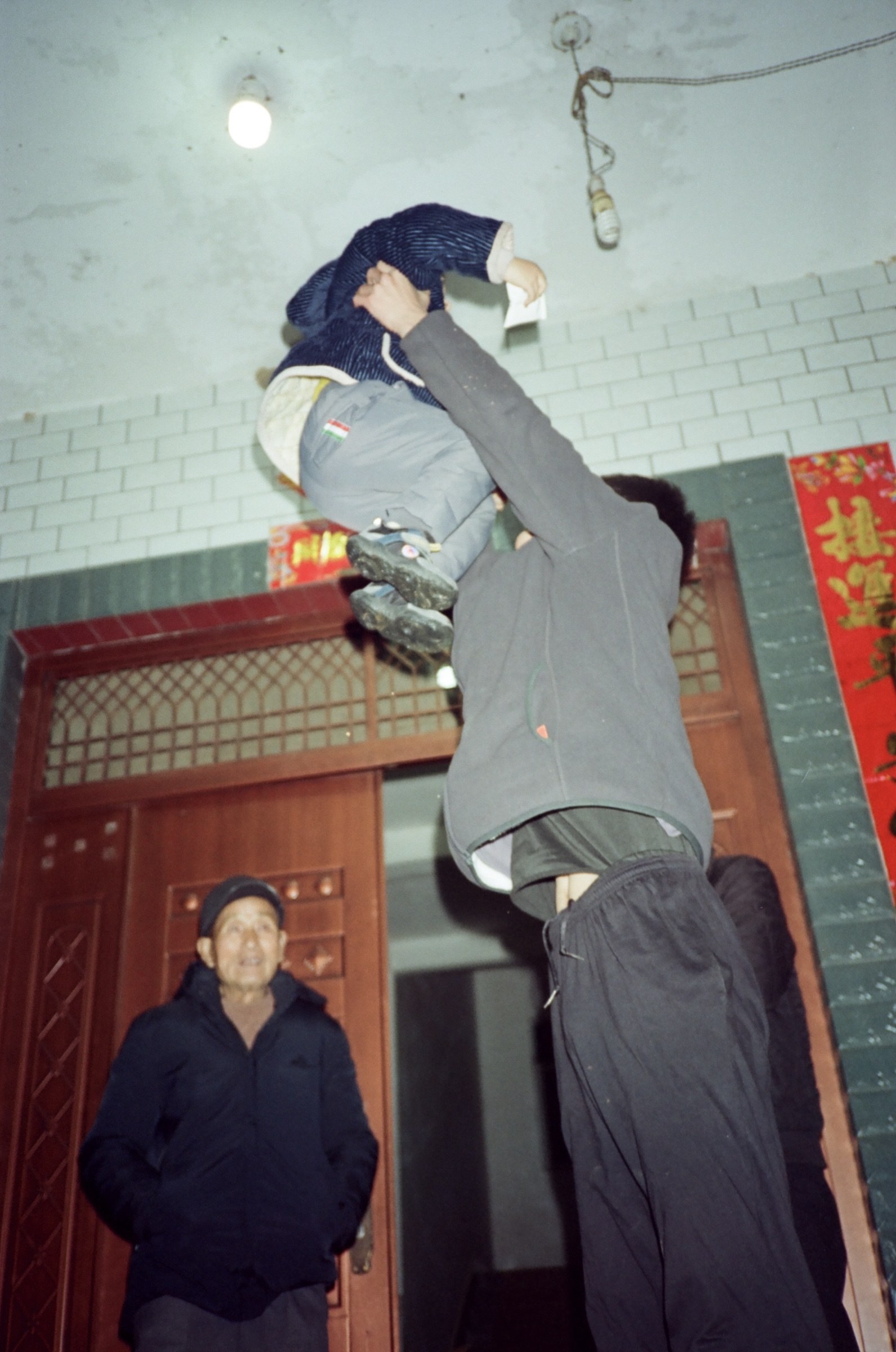门口大人把儿子高高抛起，长辈站在门边看