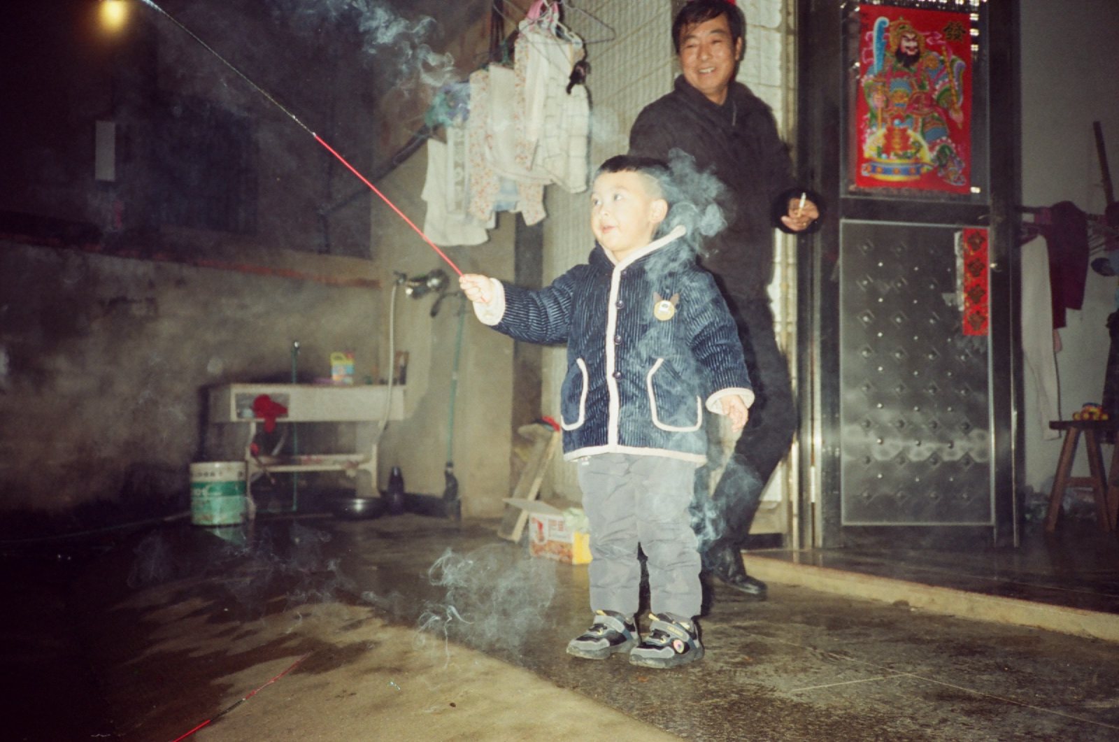 儿子拿着长长的烟花棒，身后亲戚在笑