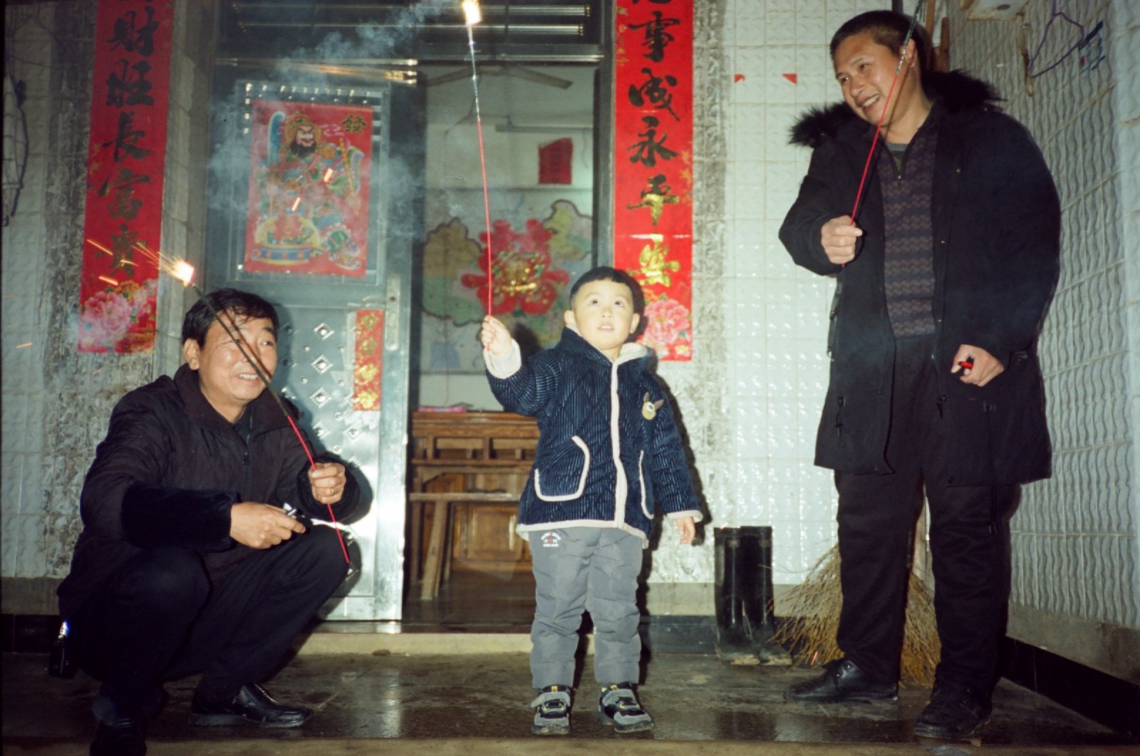 贴着门神的门前，儿子和两位亲戚一起放仙女棒