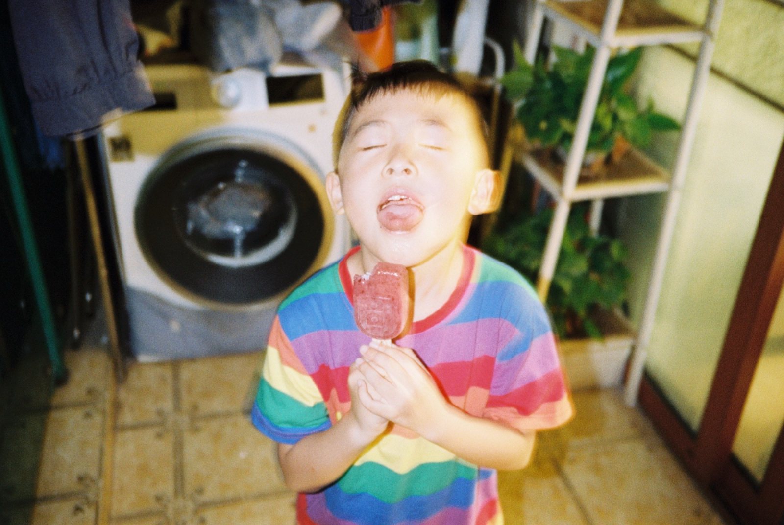 阳台洗衣机前，儿子举着冰棍吐舌头