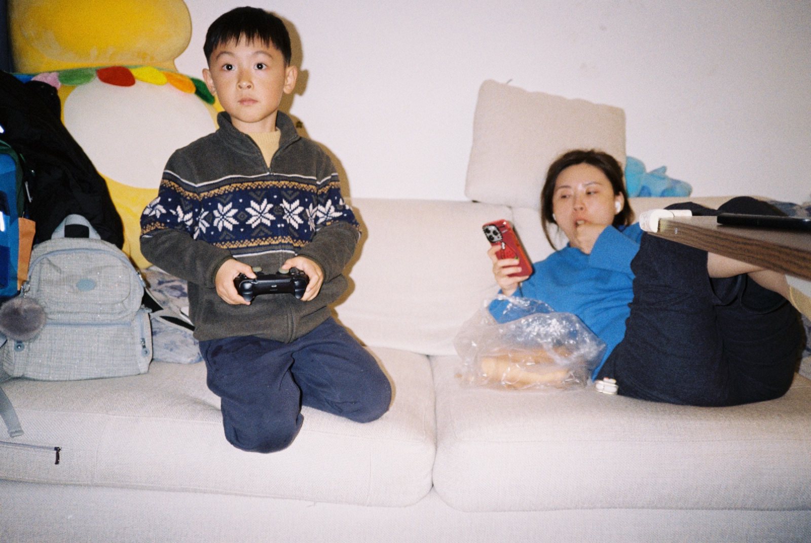 儿子跪在沙发上拿手柄，妈妈躺着看手机