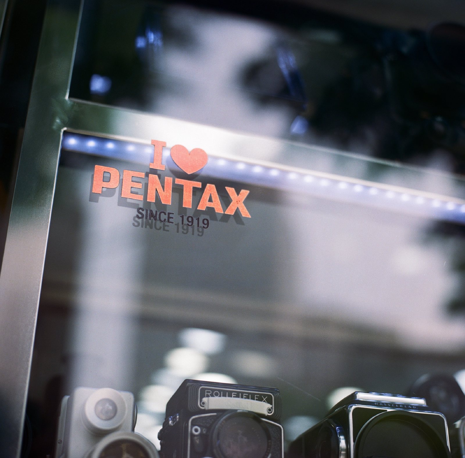 相机店橱窗，I love PENTAX 的牌子下面摆着禄莱双反和哈苏
