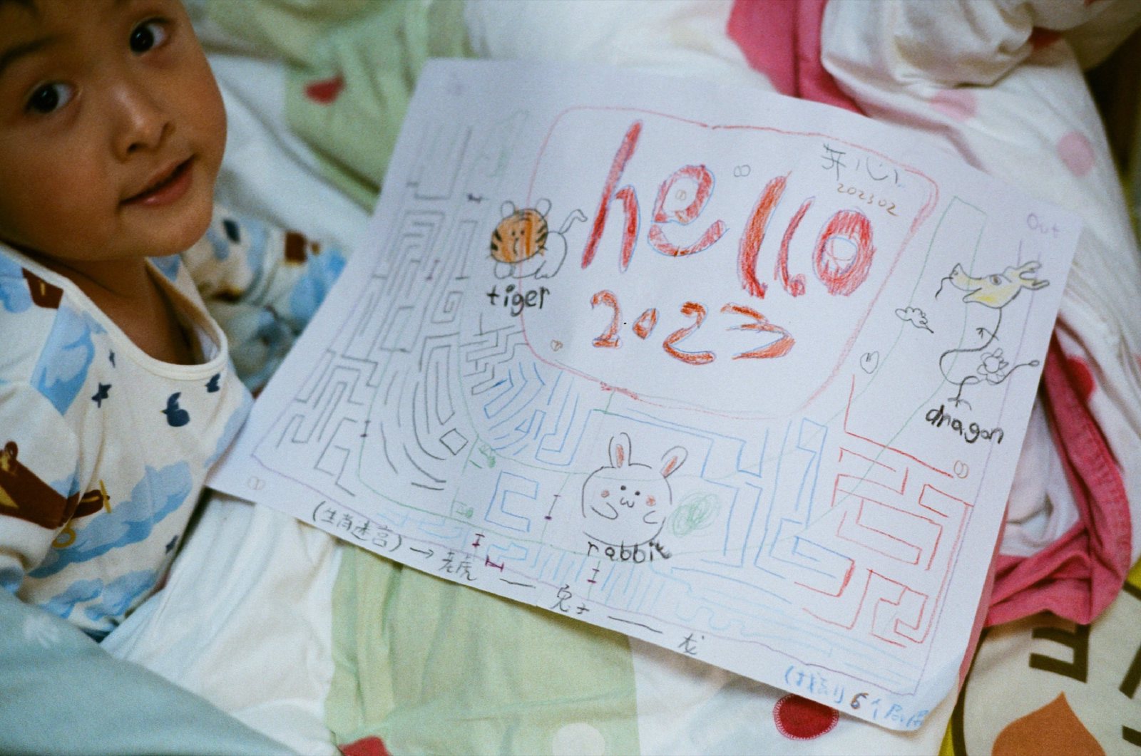 儿子躺在被子里，旁边是他画的「hello 2023」